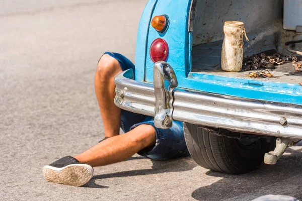 Le gambe di un uomo sotto la macchina, Vinales, Pinar del Rio, Cuba. Riparazioni auto. Primo piano . — Foto Stock