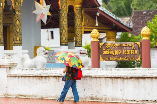 Louangphabang, Laos - 11. ledna 2017: Žena s deštníkem na pozadí chrámu. Kopírovat prostor pro text. — Stock fotografie