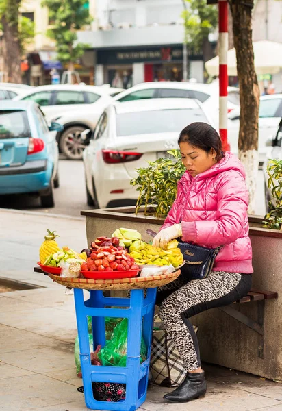 HANOI, VIETNAM - 16 DE DICIEMBRE DE 2016: Una mujer vende fruta en una calle de la ciudad. Vertical . —  Fotos de Stock