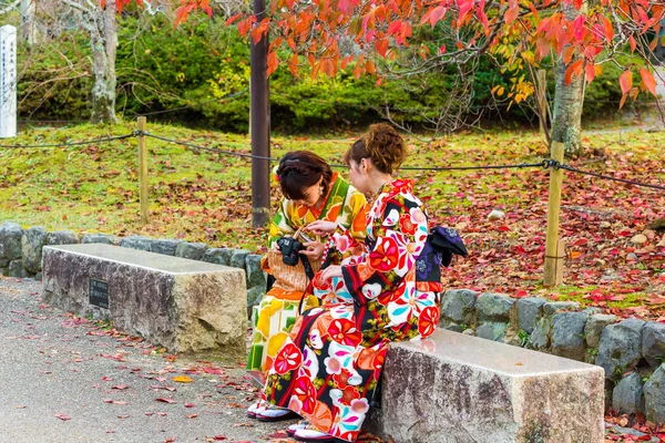 Kyoto, Japonia - 7 listopada 2017: Dwie dziewczyny w kimono siedzi na ławce w parku miejskim. Kopiować miejsca na tekst. — Zdjęcie stockowe