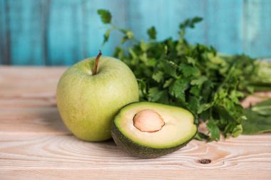 ripe avocado with parsley and apple on wooden table clipart