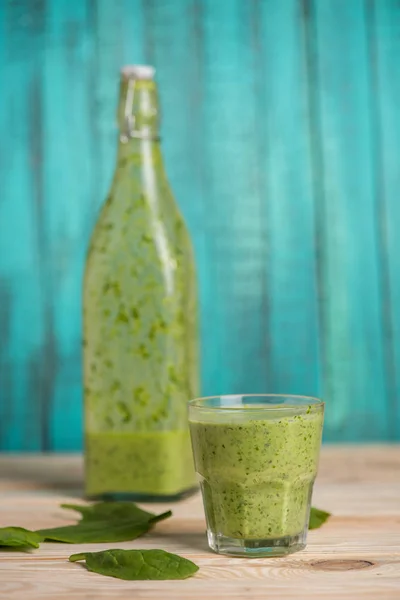 Groene bladeren en smoothie in glas en fles — Stockfoto