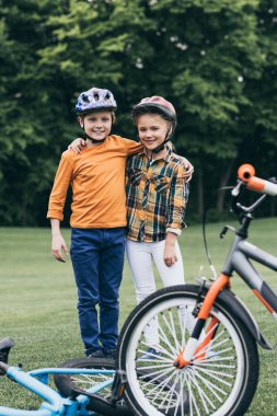 kids in helmets standing near bicycles at park clipart