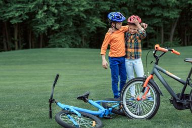 kids in helmets standing near bicycles at park clipart