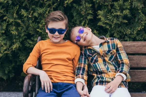 Niños sonrientes sentados en el banco en el parque —  Fotos de Stock