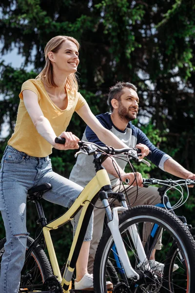 Sonriente pareja montando bicicletas en el parque —  Fotos de Stock