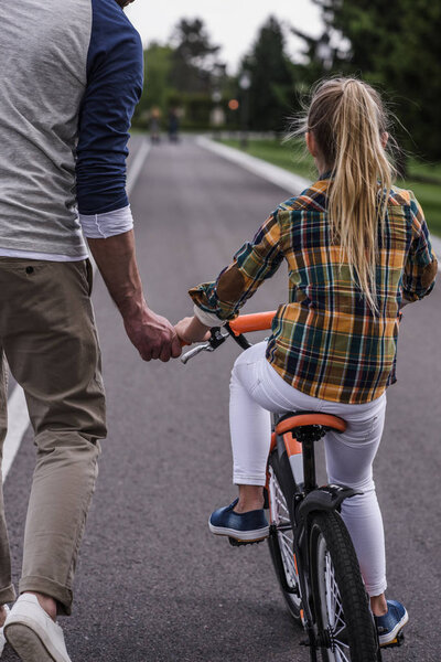 отец учит дочь кататься на велосипеде
