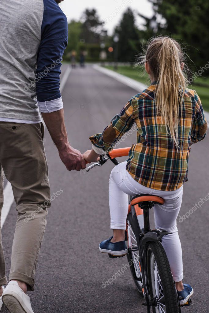 Cropped shot of father teaching his little daughter riding bicycle on asphalt road
