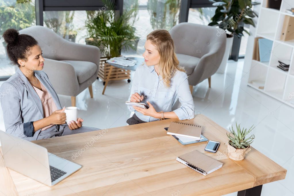 Multiethnic businesswomen discussing new business project while sitting at workplace in office