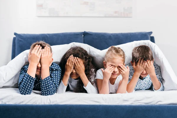 Multicultural children covering eyes on bed — Stock Photo, Image