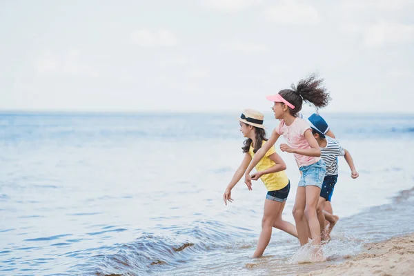 Multicultural kids throwing stones at seaside — Stock Photo, Image