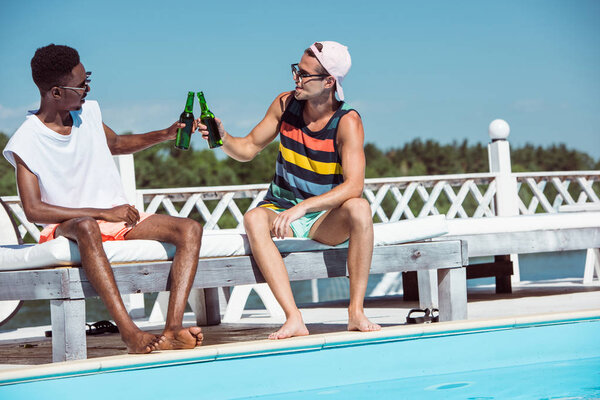 Multiethnic men with beer near pool 