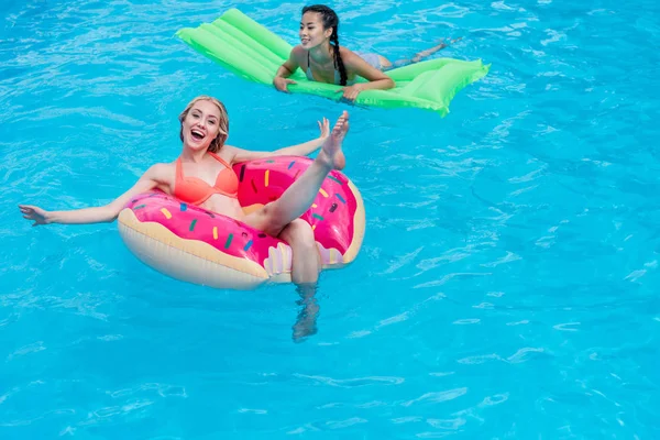 Multietniskt kvinnor på uppblåsbara madrasser i poolen — Stockfoto