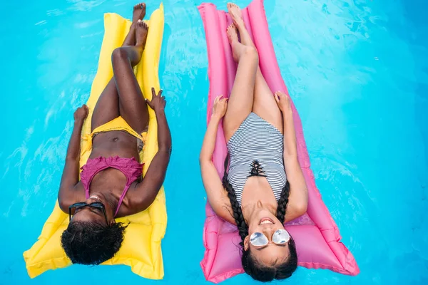 Многоэтнические женщины на надувных матрасах в бассейне — стоковое фото