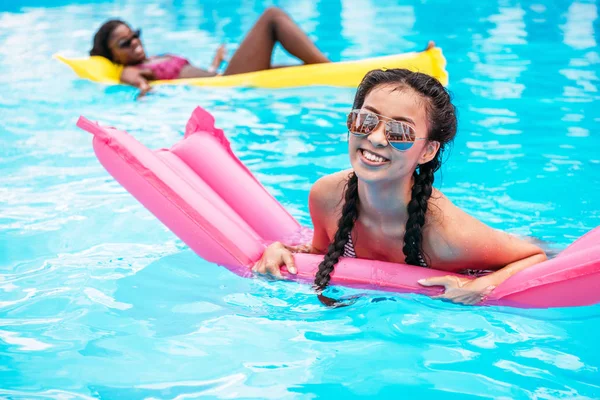 Multietniskt kvinnor på uppblåsbara madrasser i poolen — Stockfoto