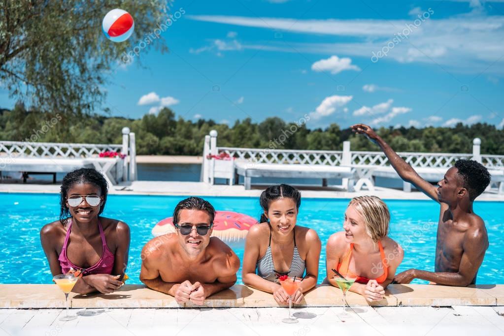 multiethnic people with cocktails in swimming pool 