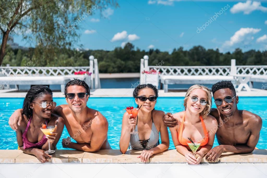 multiethnic people with cocktails in swimming pool 