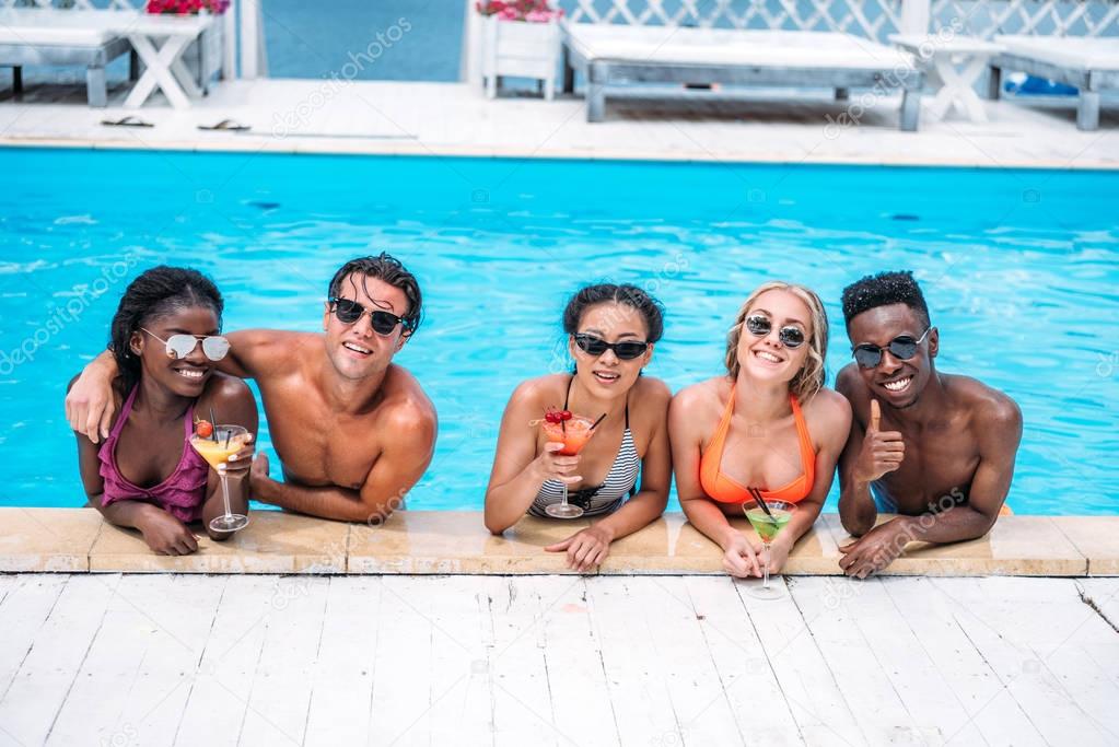 multiethnic people with cocktails in swimming pool 