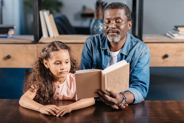 African american man reading with daughter — Stock Photo, Image