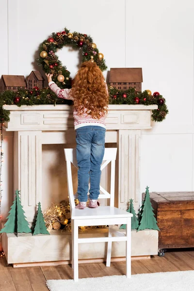 Child hanging christmas wreath at home — Stock Photo, Image