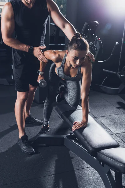 Entrenador ayudar a la mujer a hacer ejercicio con la mancuerna — Foto de Stock