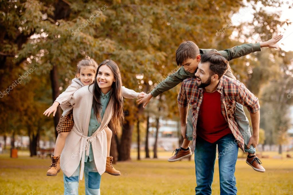 Young parents giving their children a piggyback ride in an autumn park
