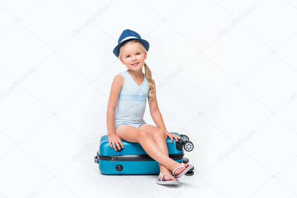child in swimsuit sitting on suitcase 