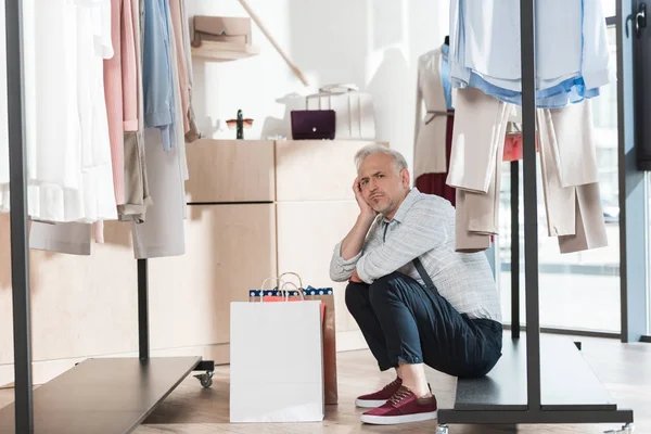 Homem sentado na prateleira da prateleira de roupas — Fotografia de Stock