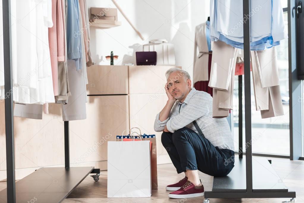 Man sitting on shelf of clothes rack