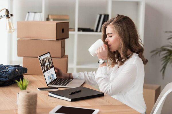 side view of businesswoman drinking coffee while working on laptop at table