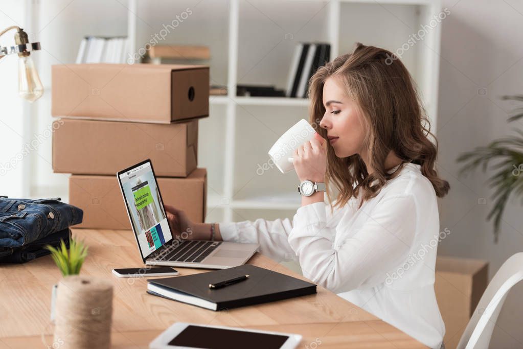 Side view of businesswoman drinking coffee while working on laptop at table