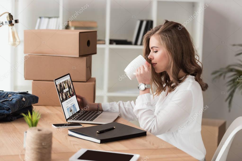 Side view of businesswoman drinking coffee while working on laptop at table