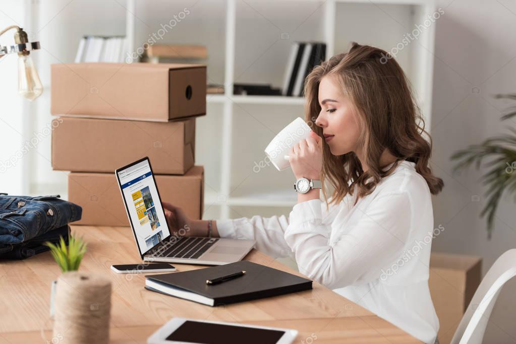 Side view of businesswoman drinking coffee while working on laptop at table