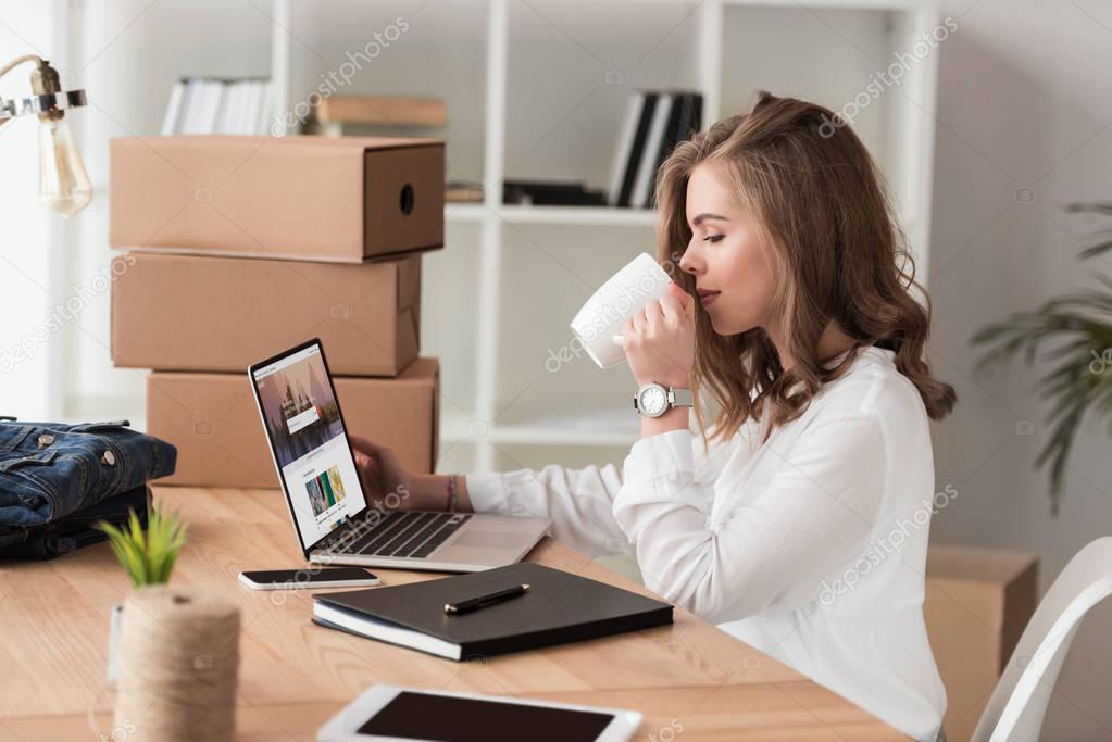 Side view of businesswoman drinking coffee while working on laptop at table