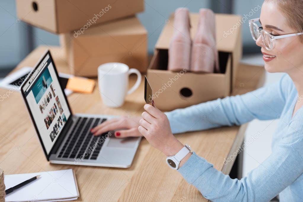 Selective focus of woman with credit card in hand looking at laptop screen at table