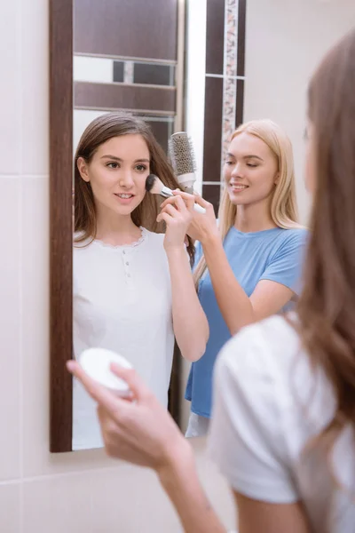 Chica Aplicando Base Polvo Con Cepillo Maquillaje Amigo Peinando Cabello — Foto de stock gratis