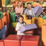 Padres felices mirando a la pequeña hija edificio castillo con bloques de colores en el centro del juego