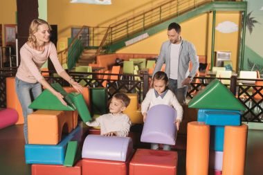 İki çocukla renkli oynamaktan mutlu aile oyun merkezinde engeller 