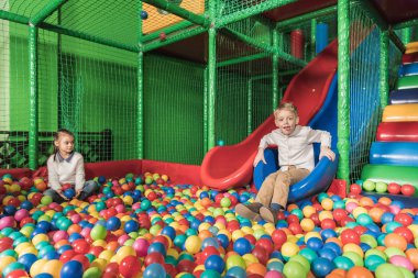 happy siblings playing in pool with colorful balls at entertainment center clipart