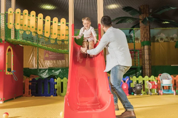 Visão Traseira Pai Olhando Para Pequeno Filho Brincando Slide Centro — Fotografia de Stock