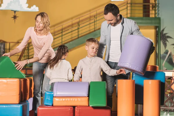 愉快的父母与女儿和儿子一起演奏五颜六色的块在娱乐中心 — 免费的图库照片