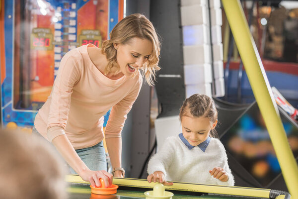 selective focus of happy mother and daughter playing air hockey in entertainment center 