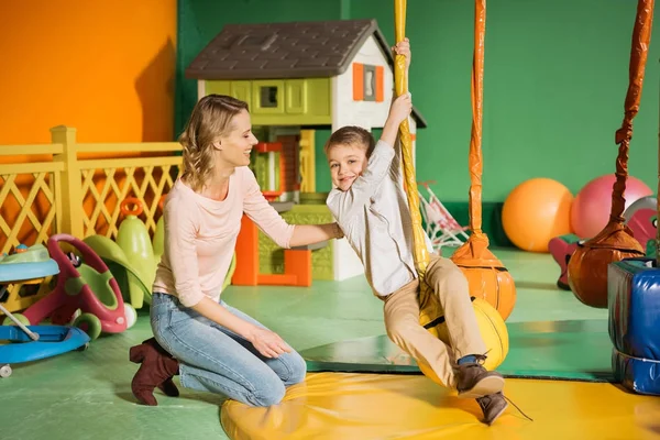 Happy Mother Looking Cute Smiling Son Swinging Entertainment Center — Stock Photo, Image