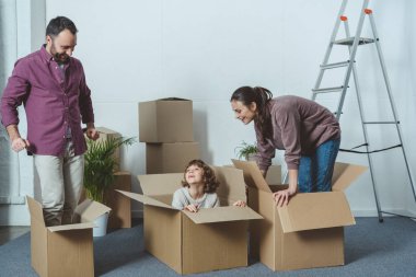 happy parents looking at son sitting in cardboard box during relocation clipart