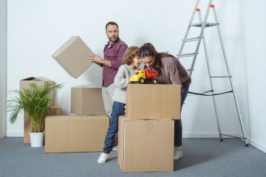 family with one child packing cardboard boxes while moving home  clipart