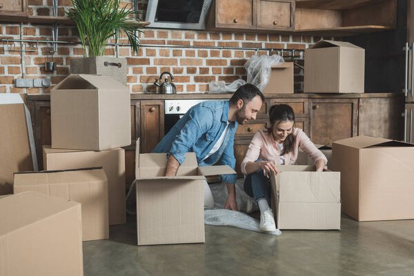 smiling young couple unpacking boxes while moving in new house