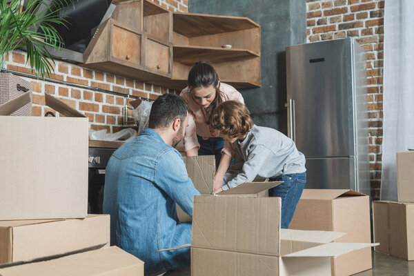 family with one child unpacking cardboard boxes in new apartment