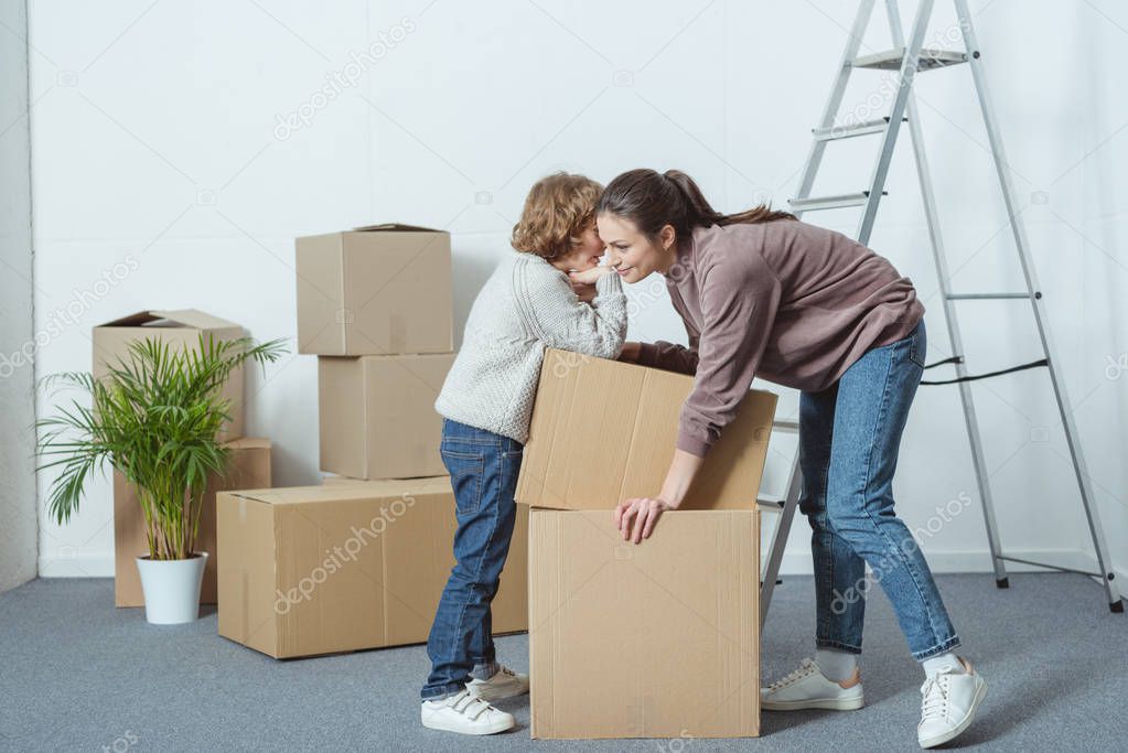 little boy whispering something to mother while packing cardboard boxes together