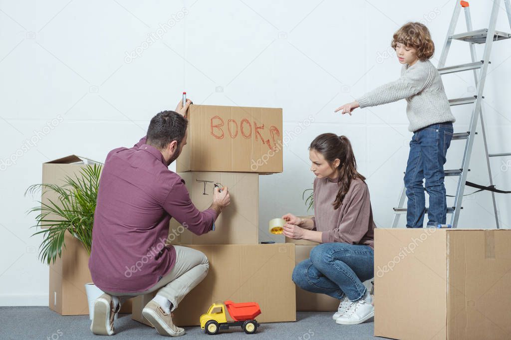 parents packing boxes and son pointing with finger during relocation