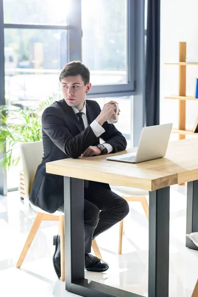 Jovem Empresário Bebe Café Enquanto Trabalha Laptop Escritório Moderno — Fotografia de Stock